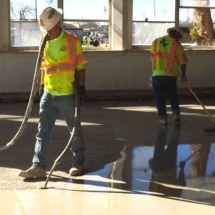 Two men in reflective jackets are cleaning a floor.